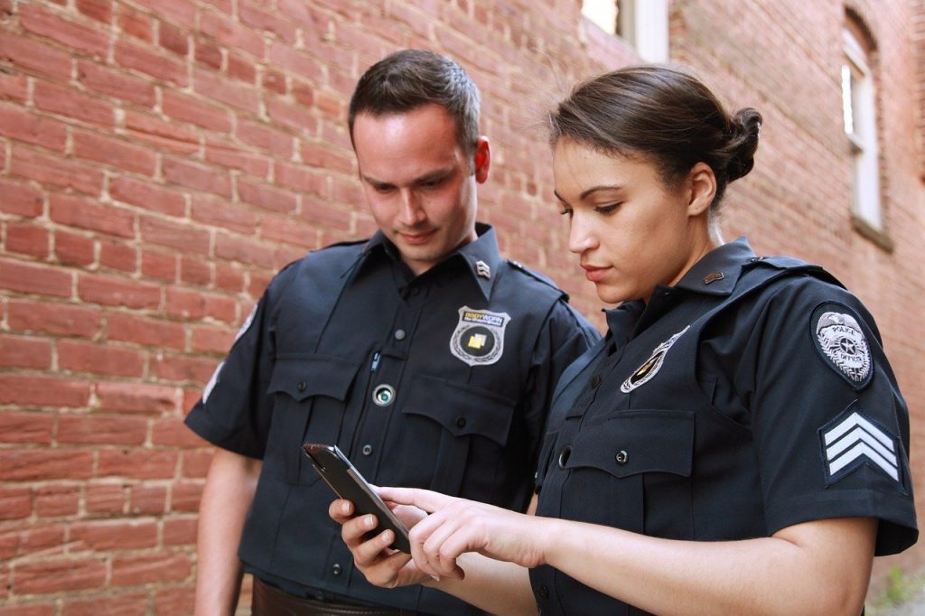 A woman and a man police officer standing outside looking at a phone.