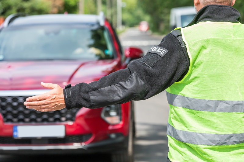 Policeman in a reflective vest extends his hand to stop a red car